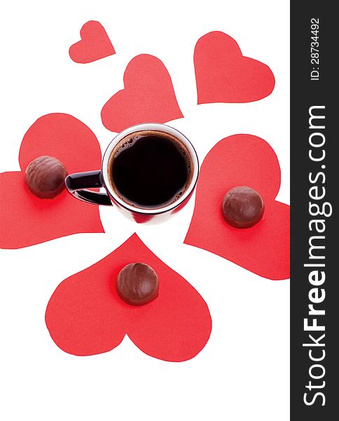 Round chocolate candy in the heart of red paper and black coffee on a white background. Round chocolate candy in the heart of red paper and black coffee on a white background