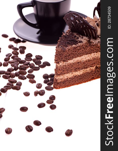 Piece of cake on the background of a black сup with saucer and scattered grain coffee. Piece of cake on the background of a black сup with saucer and scattered grain coffee