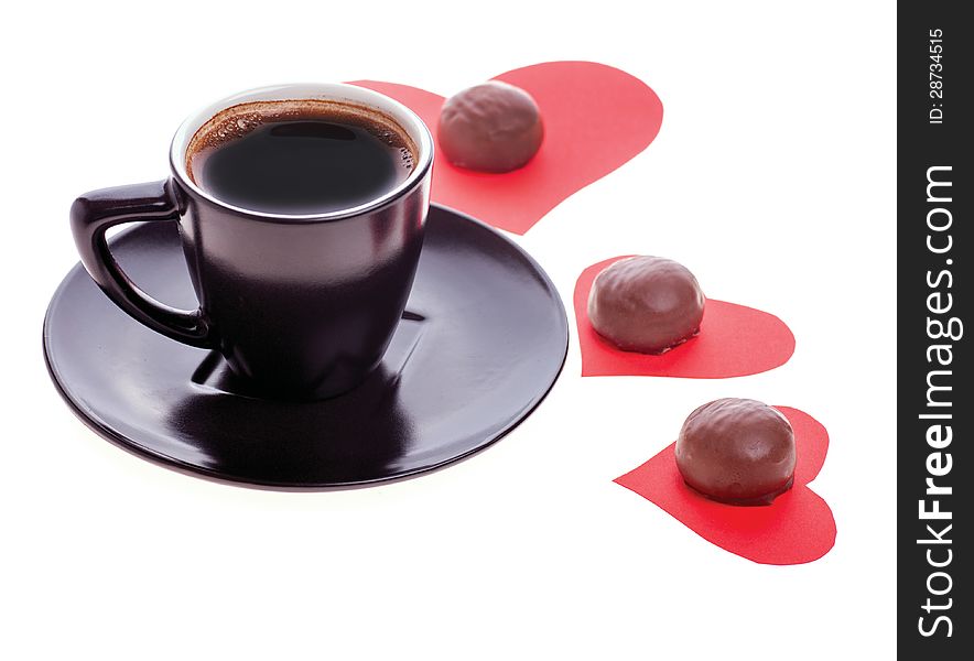 Round chocolate candy in the heart of red paper and black coffee on a white background. Round chocolate candy in the heart of red paper and black coffee on a white background