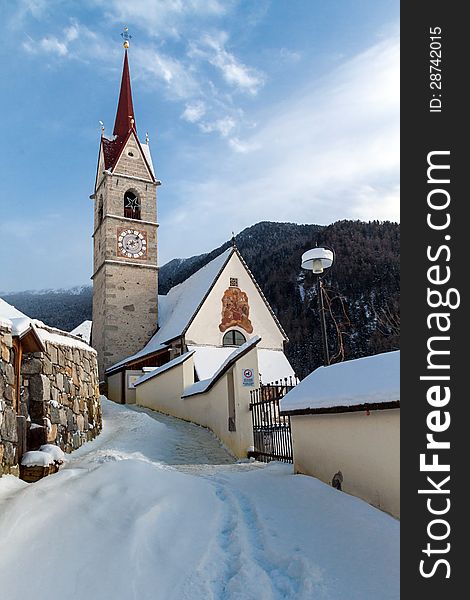 A wintertime view of a small church with a tall steeple in the Sud Tyrol, Italy.