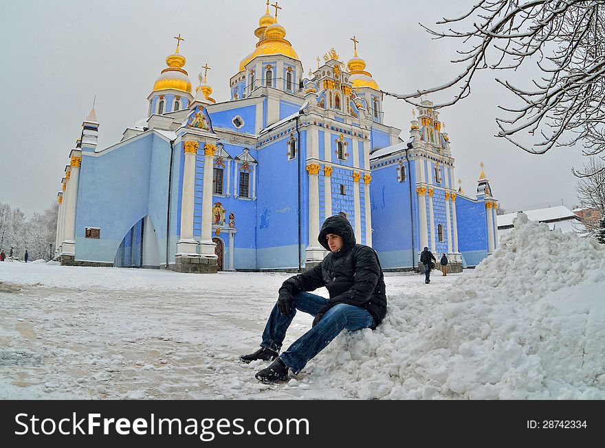 Against church with gold domes the young man in the winter sits. Against church with gold domes the young man in the winter sits