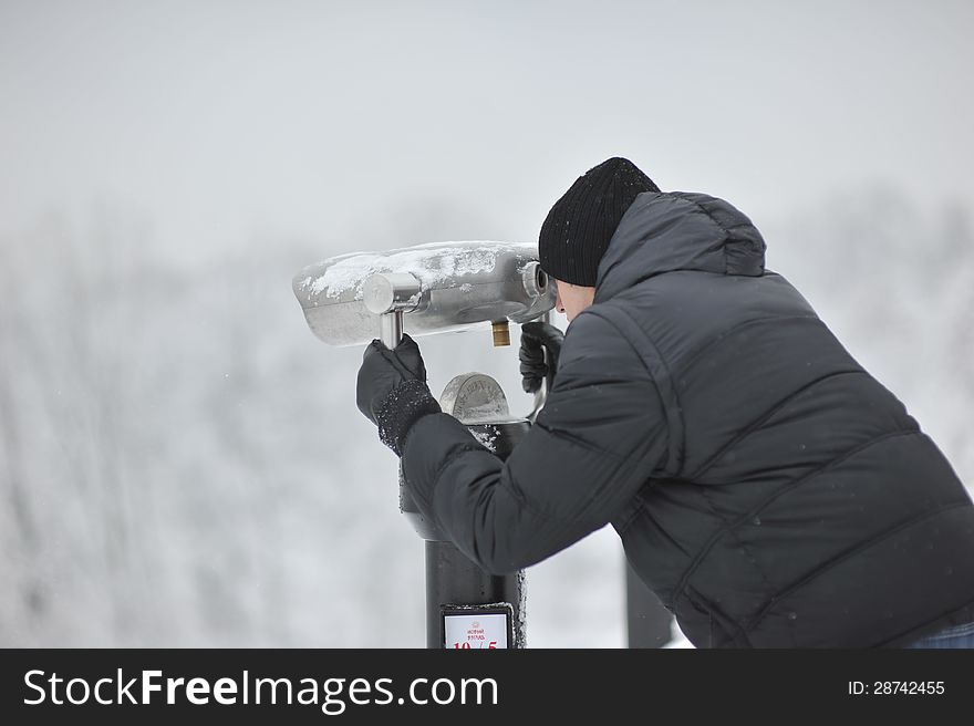 Winter man in a black jacket and hat looking through binoculars. Winter man in a black jacket and hat looking through binoculars