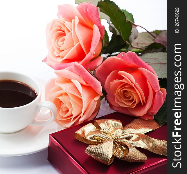 Flowers, cup of coffee and sweets. Close up red gift box with gold bow