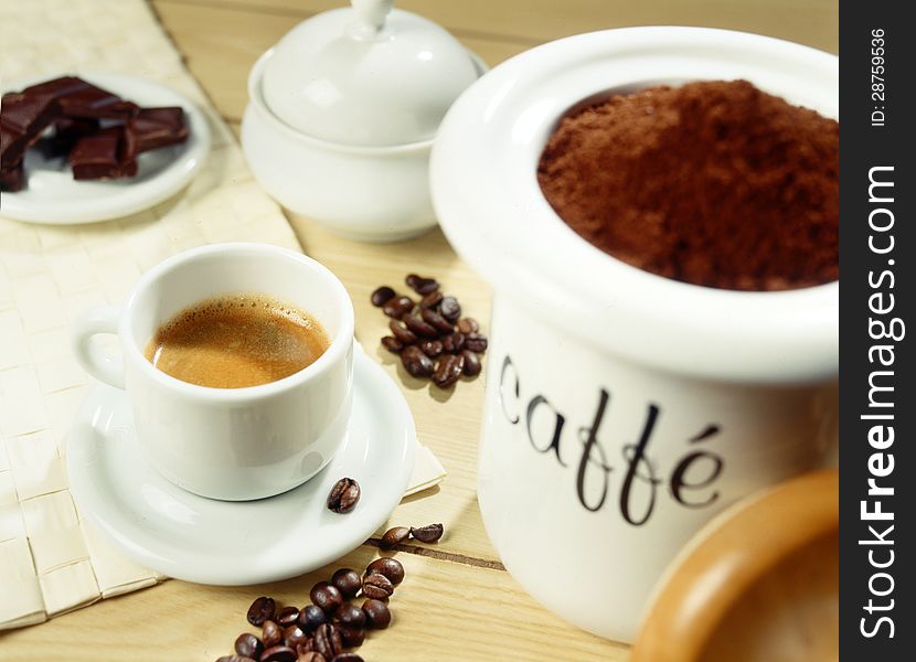 Container of aromatic freshly ground coffee beans alongside a rich freshly brewed cup of espresso and whole beans