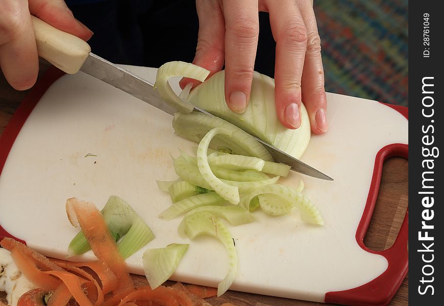 A piece of fennel is cut in thin stripes in order to make a vegetable stew. A piece of fennel is cut in thin stripes in order to make a vegetable stew