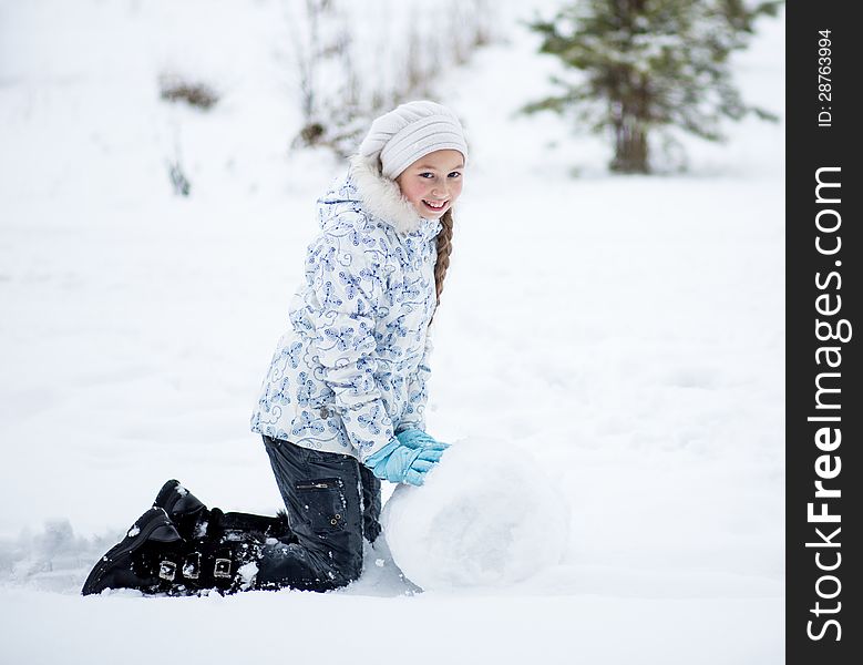Child making snowman in winter park