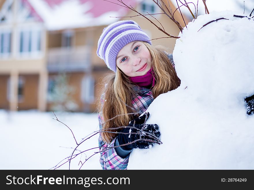 Young girl making snowman outdoors 
in front of house. Young girl making snowman outdoors 
in front of house