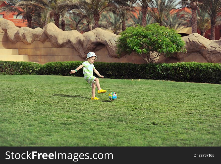 On a green grassy field the child plays football. On a green grassy field the child plays football