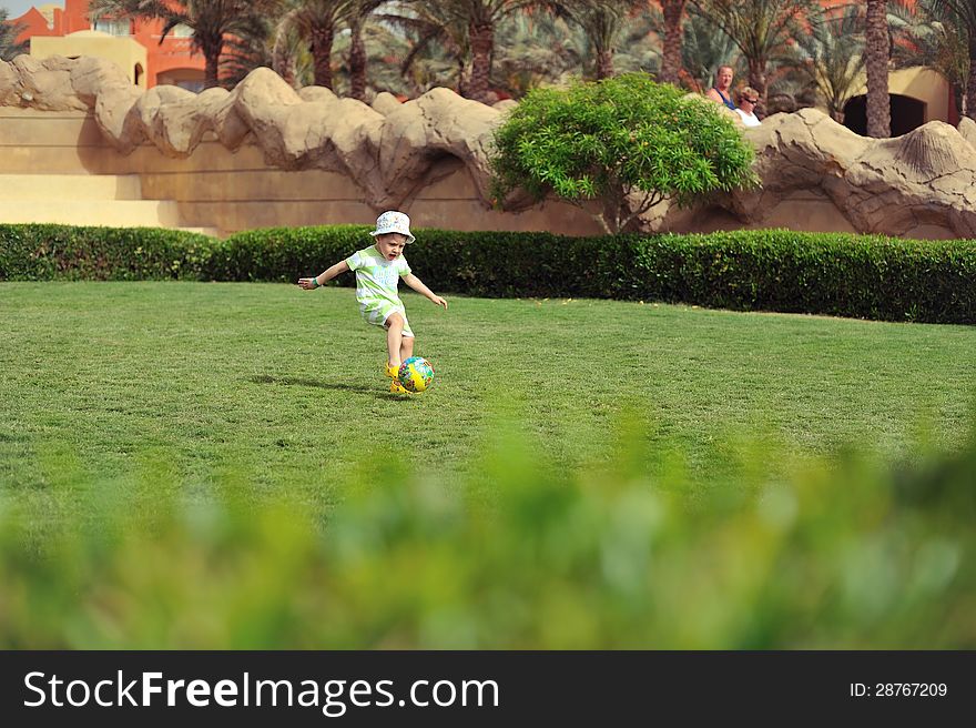 On a green grassy field the child plays football. On a green grassy field the child plays football