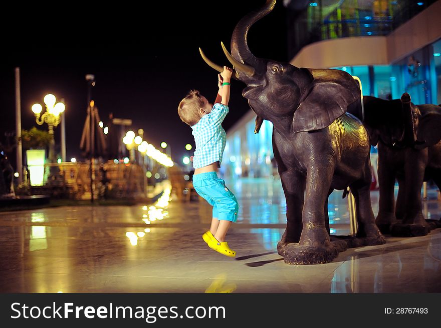 In the evening on the street a boy playing with an elephant sculpture. In the evening on the street a boy playing with an elephant sculpture