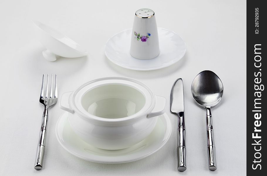 Tureen, salt shaker and cutlery served on a white tablecloth