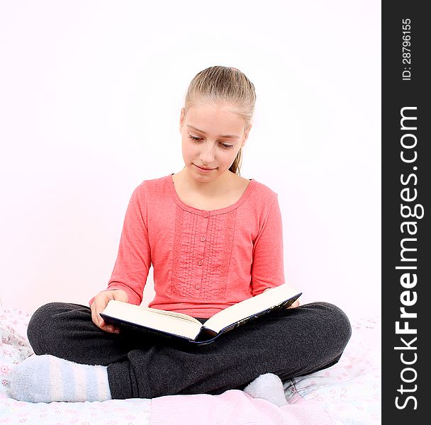 Blond girl reads interesting book sitting on bed