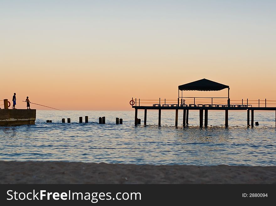 Sundown on sea. Two fisherman on pier