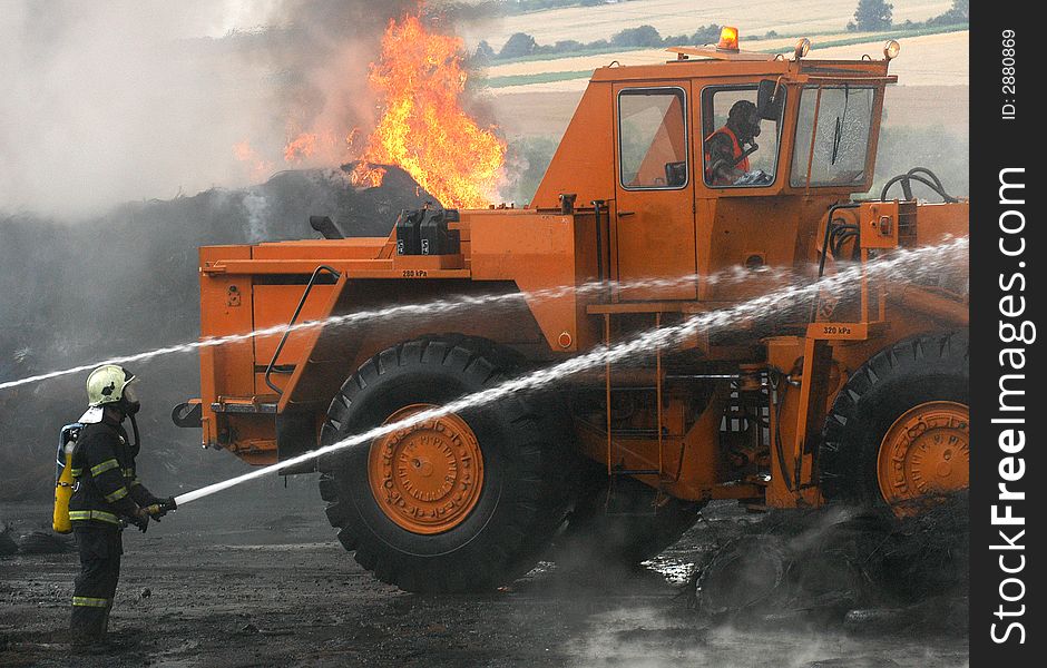 Two Firemen and a digger fighting the fire of tires