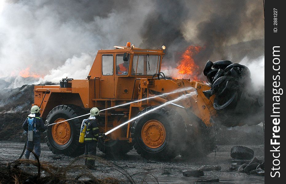 Two Firemen and a digger fighting the fire of tires