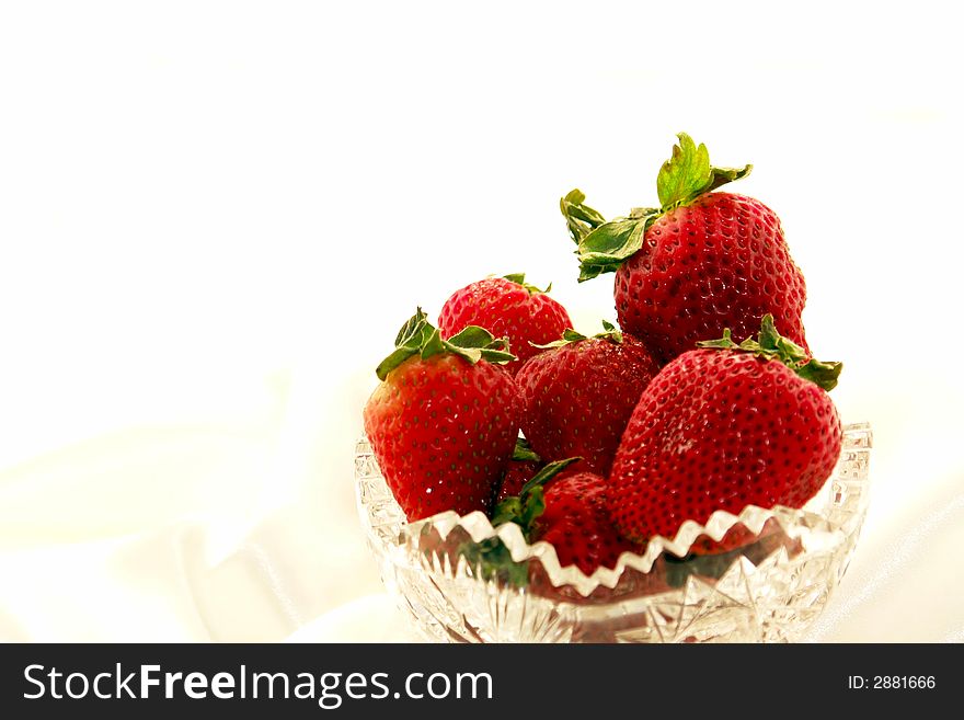 Scrumptuous red strawberries in a crystal bowl against a white satin background. Scrumptuous red strawberries in a crystal bowl against a white satin background