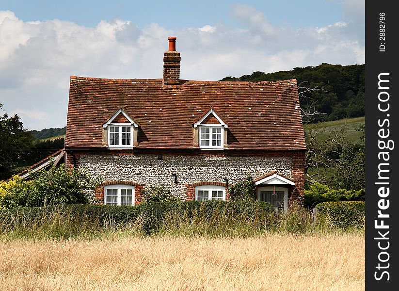 Brick and Flint Cottage in a Rural Village in England with a hedge and Meadow to the front