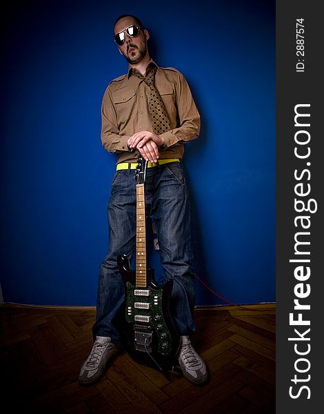 Guitar player in a cool pose, leaning against a blue wall. Guitar player in a cool pose, leaning against a blue wall.