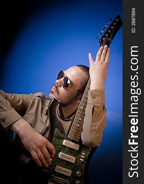 Guitar player with sunglasses in studio, posing with his guitar, broader view. Guitar player with sunglasses in studio, posing with his guitar, broader view.