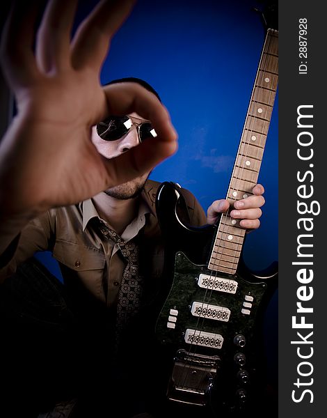 Guitar player with sunglasses in studio, giving an OK sign. Focus on guitarist. Guitar player with sunglasses in studio, giving an OK sign. Focus on guitarist.