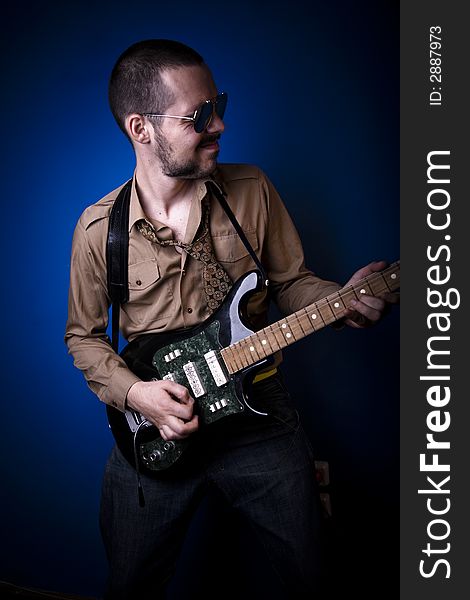 Guitar player with sunglasses in studio, jamming. Blue background. Guitar player with sunglasses in studio, jamming. Blue background.