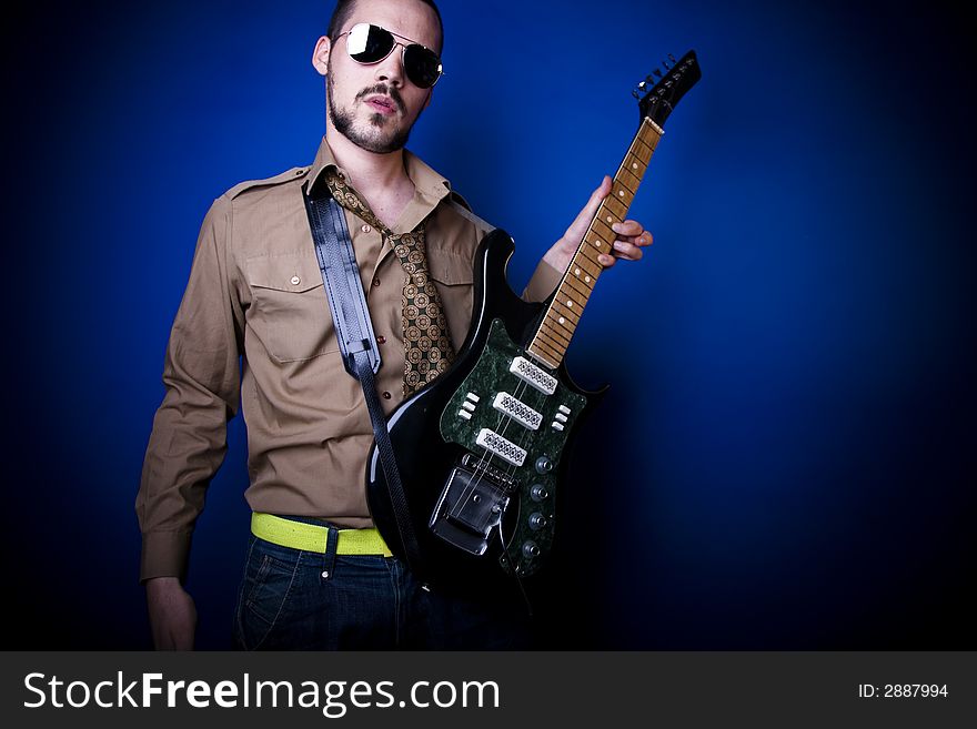 Guitar player with sunglasses in studio against a blue wall.