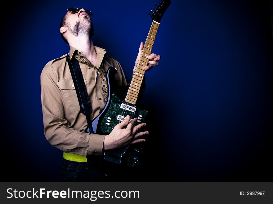 Alternative rocker playing intensely on his guitar. Dark blue background and vignette. Alternative rocker playing intensely on his guitar. Dark blue background and vignette.