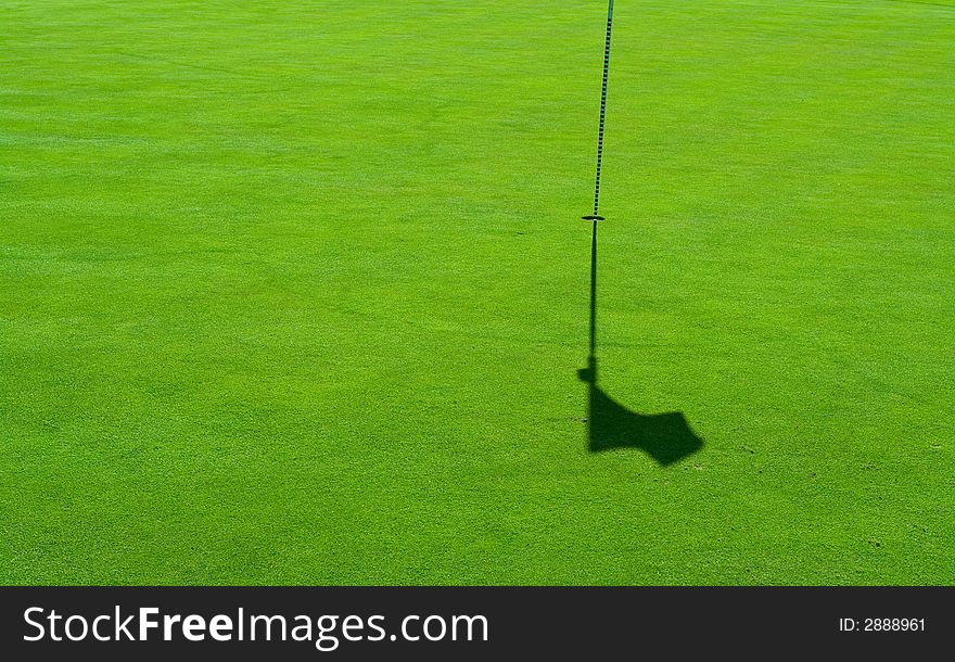 A hole with a flag pole and a shadow on a perfect green grass. A hole with a flag pole and a shadow on a perfect green grass