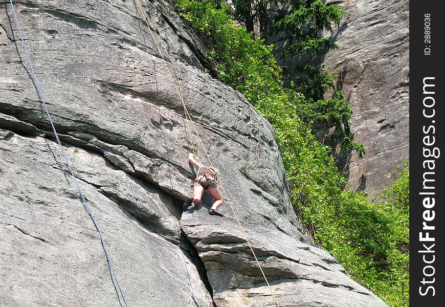 Young woman begins her climb on steep rock face. Young woman begins her climb on steep rock face.