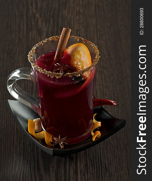 Glass of Mulled Wine and Spices with Cinnamon Stick, Orange, Anise Star and Sugar on Black Saucer closeup Wood background