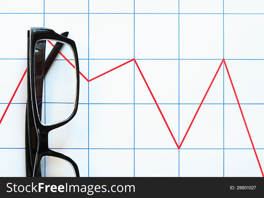 Business concept. Eyeglasses lying on paper background with red chart. Business concept. Eyeglasses lying on paper background with red chart