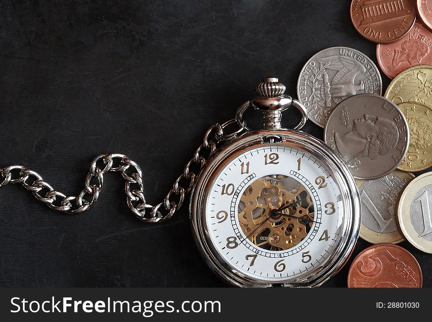 Closeup of pocket watch near set of coins on dark metal background. Closeup of pocket watch near set of coins on dark metal background