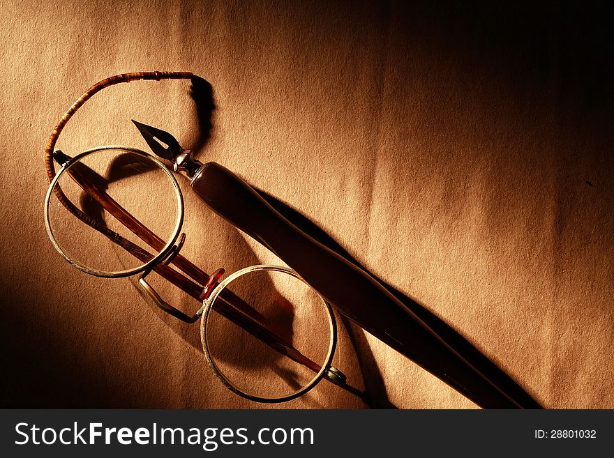 Old spectacles and ink pen on paper surface under beam of light. Old spectacles and ink pen on paper surface under beam of light