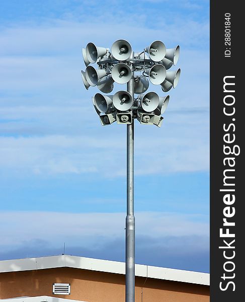 Many different speakers on a pylon over clody blue sky background