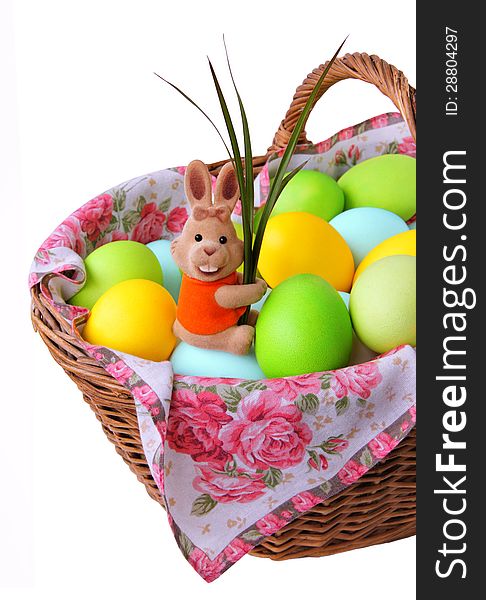 Easter bunny sitting in a basket with colored eggs and holding green leaves. Isolated on a white background. Easter bunny sitting in a basket with colored eggs and holding green leaves. Isolated on a white background.
