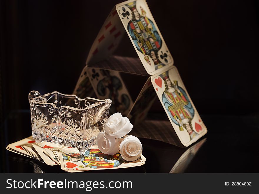 Small crystal sugar cup, some wax roses and a pyramid of playing cards.