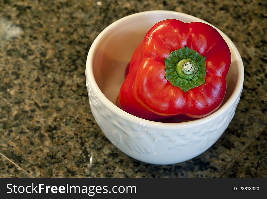 Red bell pepper in a white bowl on a granite countertop. Red bell pepper in a white bowl on a granite countertop.