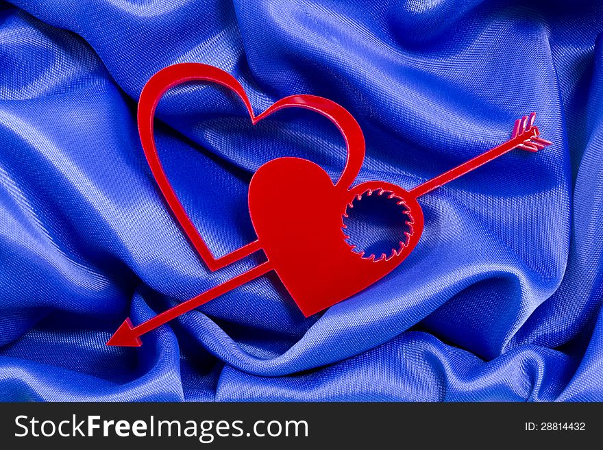 Two love hearts shapes with arrow and cogwheel hole inside of one of them on a blue silk background. Two love hearts shapes with arrow and cogwheel hole inside of one of them on a blue silk background