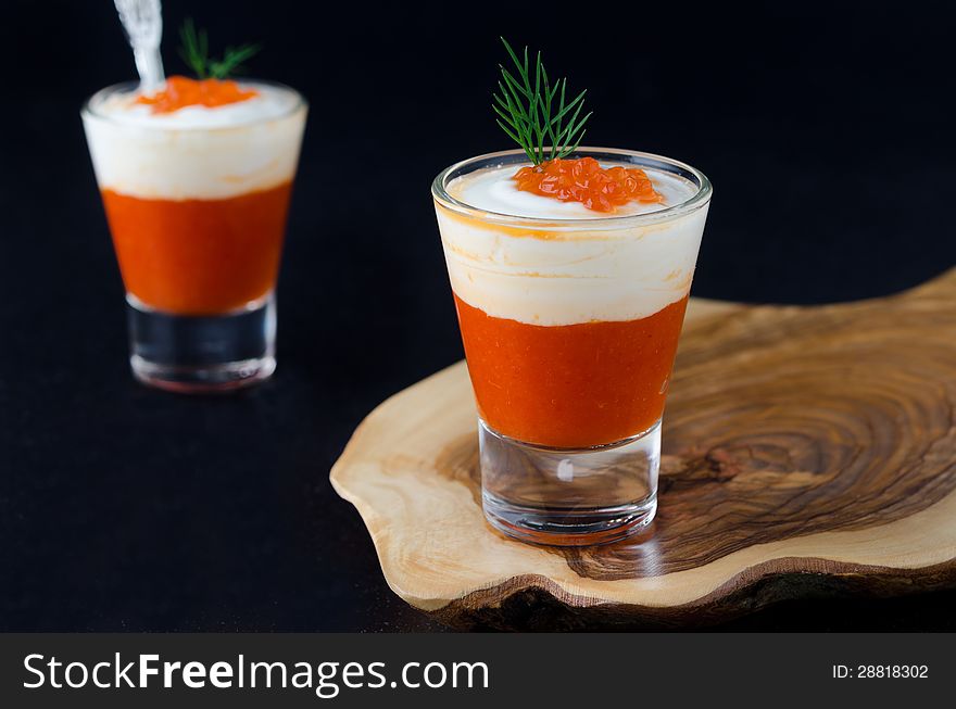 Appetizer of sweet pepper, cream and red caviar in a glass goblet on a wooden board on a black background