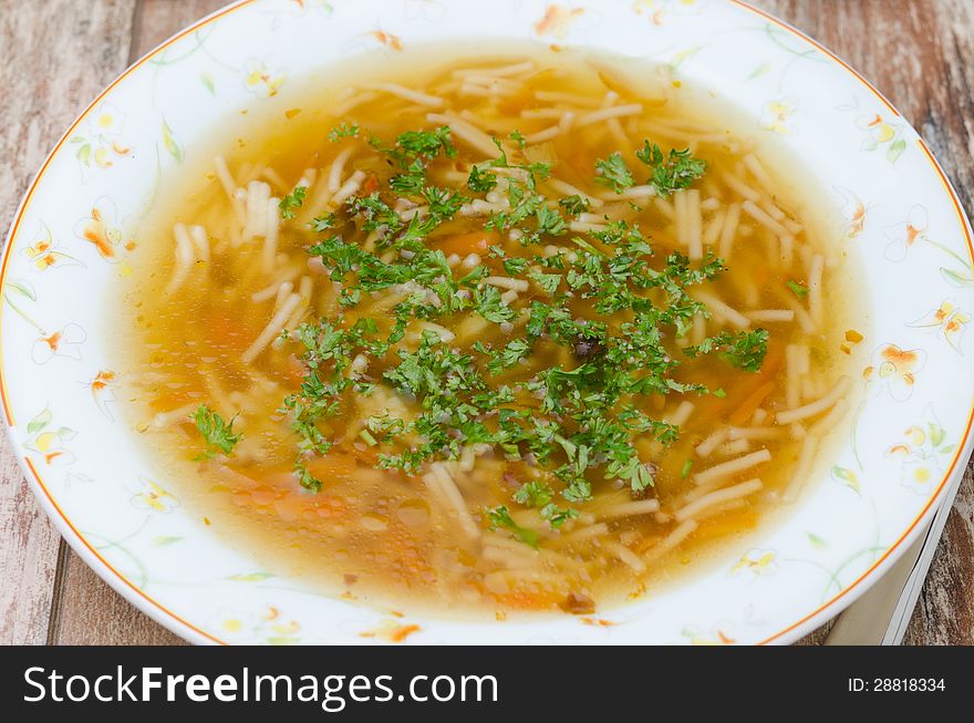 Chicken soup with noodles and carrots on a wooden table closeup. Chicken soup with noodles and carrots on a wooden table closeup