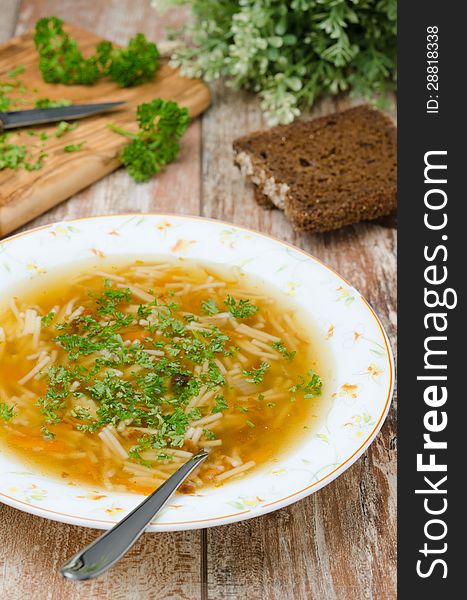 Chicken soup with noodles and carrots with fresh herbs on the plate, vertical. Chicken soup with noodles and carrots with fresh herbs on the plate, vertical