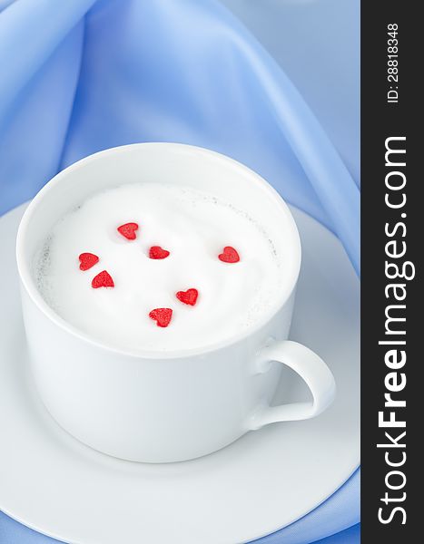 Cup of hot milk foam and sugar hearts on a blue background