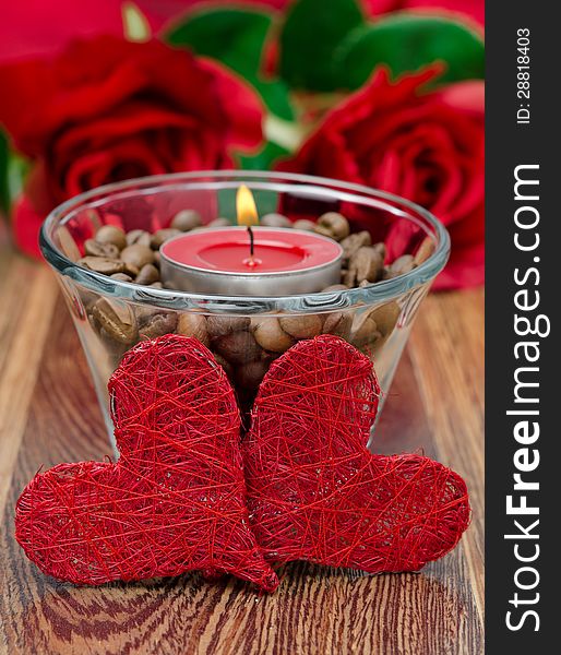 Red candle in a glass cup with coffee beans and two hearts for Valentine's Day closeup