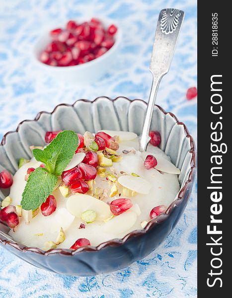 Semolina dessert with pomegranate seeds and pistachios in a bowl on a blue background closeup