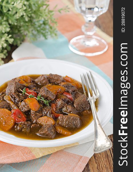 Stew of beef with vegetables and prunes in a plate, vertical