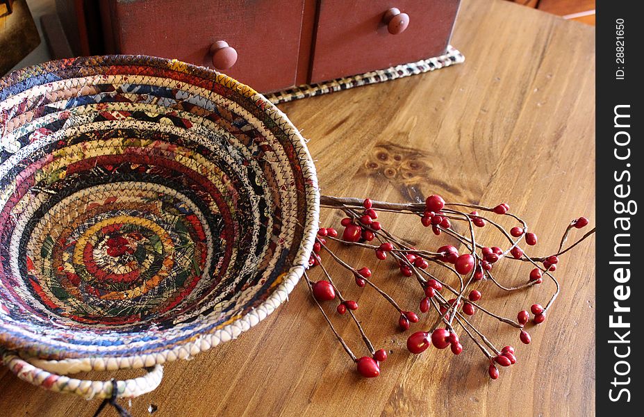 Colorful braided basket handcrafted and set on wood table with chest and red berries. Colorful braided basket handcrafted and set on wood table with chest and red berries.