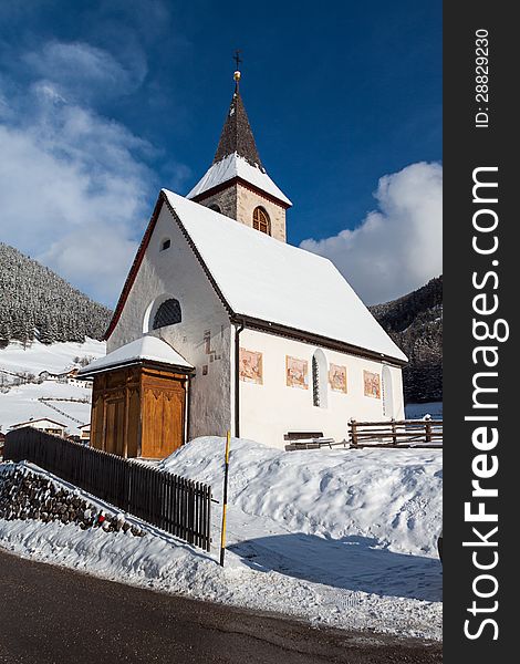 A wintertime view of a small church with a tall steeple in Montassilone, Sud Tyrol