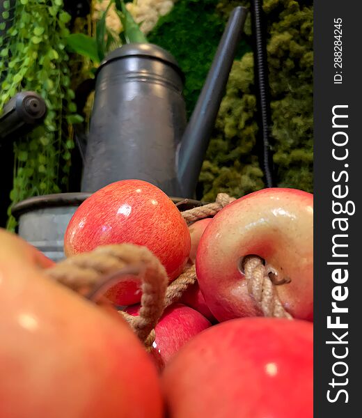 Bright red apples with rope in front of dark objects and green plants