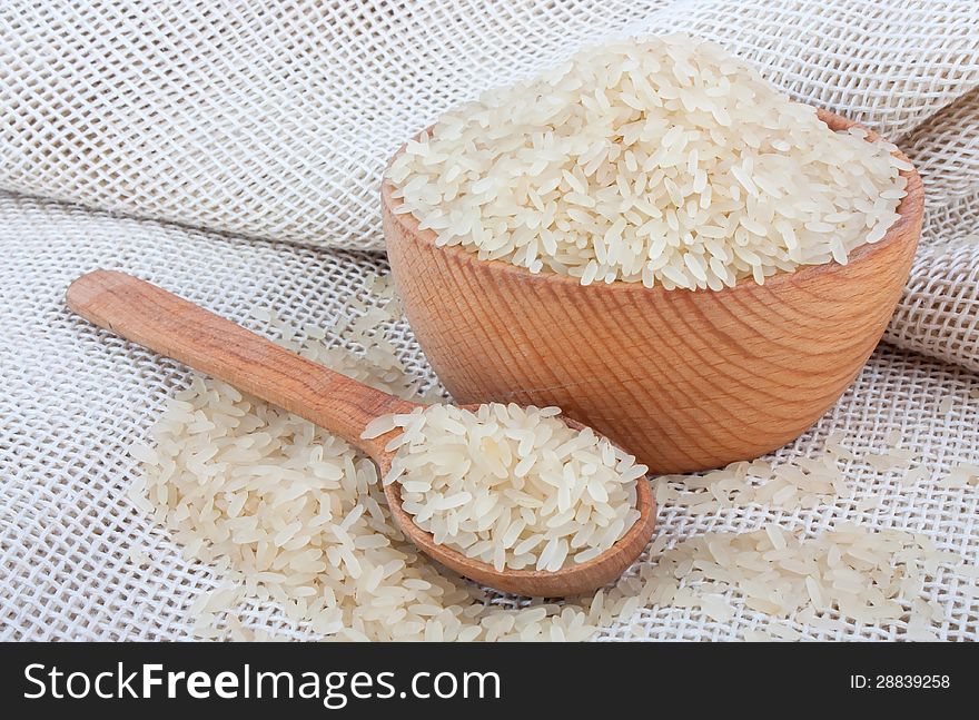 Raw white rice in wooden bowl and spoon on burlap, food ingredient photo