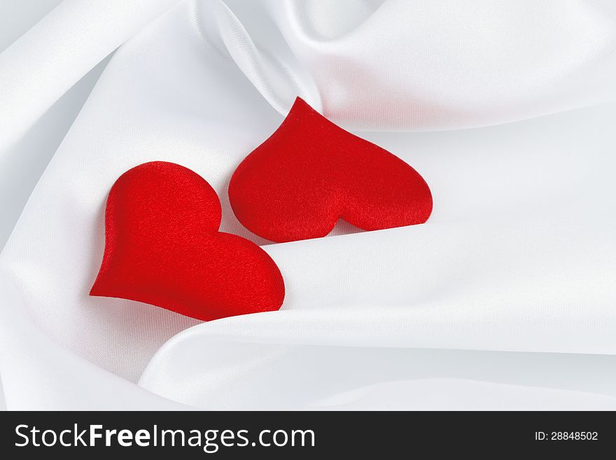 Two red hearts on white silk background